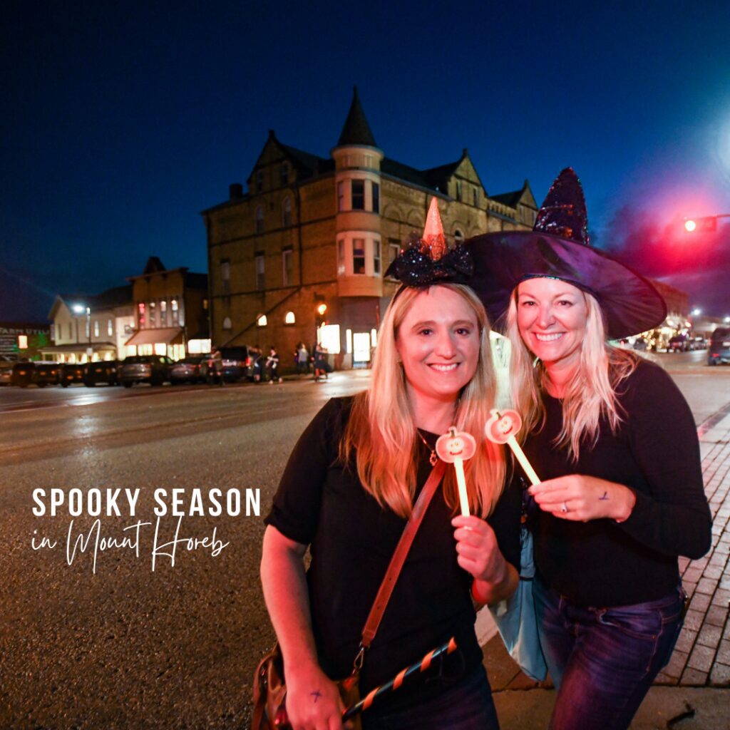 two women dressed as witches pose in front of mount horeb's trollway on witches night out