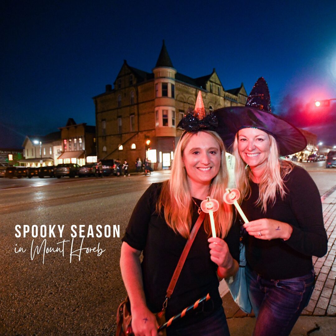 two women dressed as witches pose in front of mount horeb's trollway on witches night out